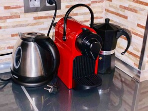 A kitchen with a red coffee machine, a black electric kettle, and a black coffee pot on a countertop.