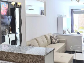 A modern living room with a beige sofa, a glass coffee table, and a kitchen area with a white countertop. - Modern Apartment with Terrace, Near Beaches & Train Station, Fully Equipped (Torremolinos)
