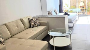 En moderne stue med en beige sofa, et glasbord og udsigt til en udendørs patio.