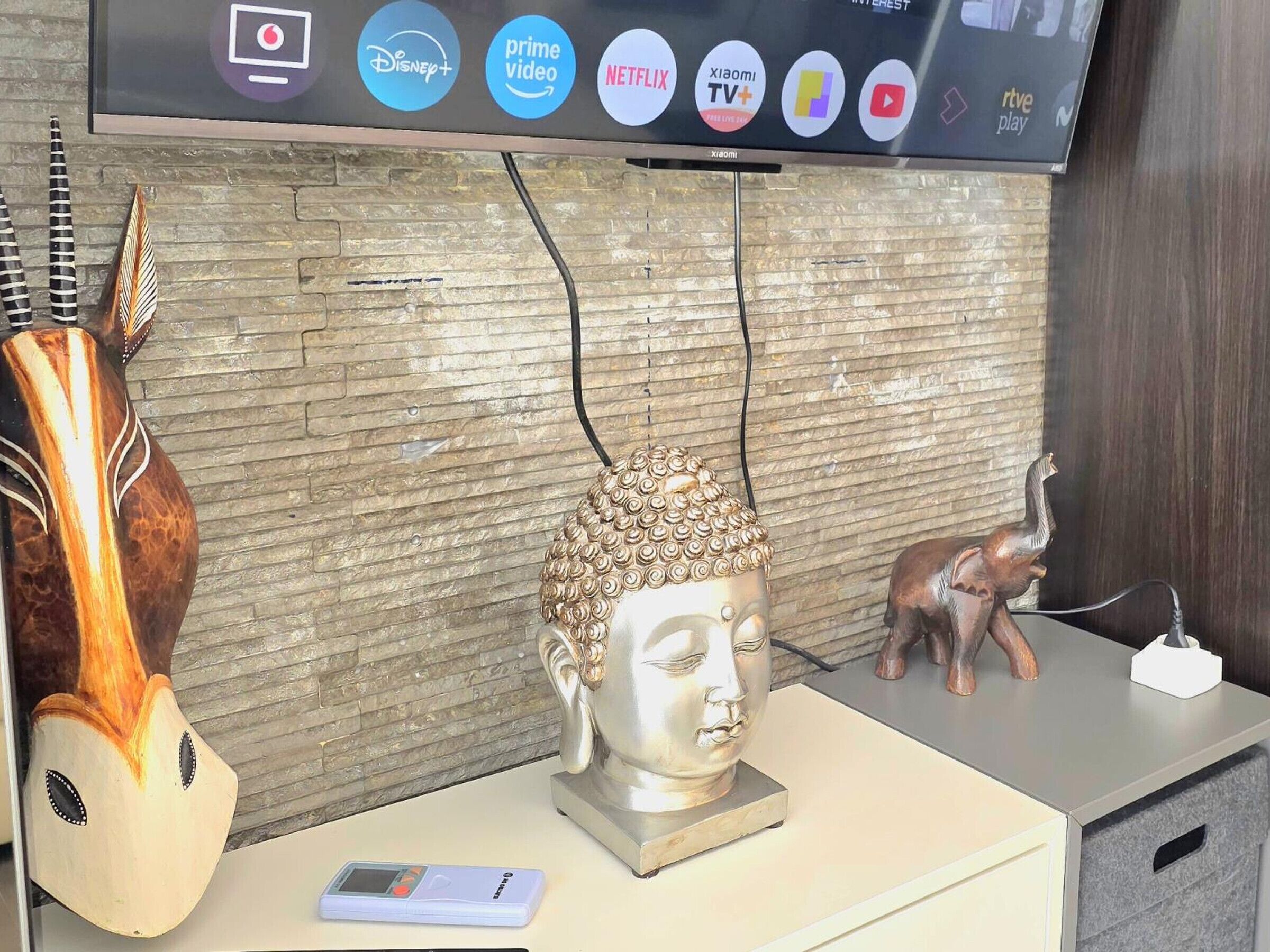 A room with a television displaying streaming service logos, a Buddha statue, a small elephant figurine, and a smartphone on a table.