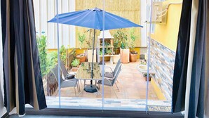 En balkon med et bord, stole, en blå parasol og krukker med planter.
