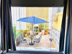Ein Balkon mit Tisch und Stühlen, einem blauen Sonnenschirm und Topfpflanzen.