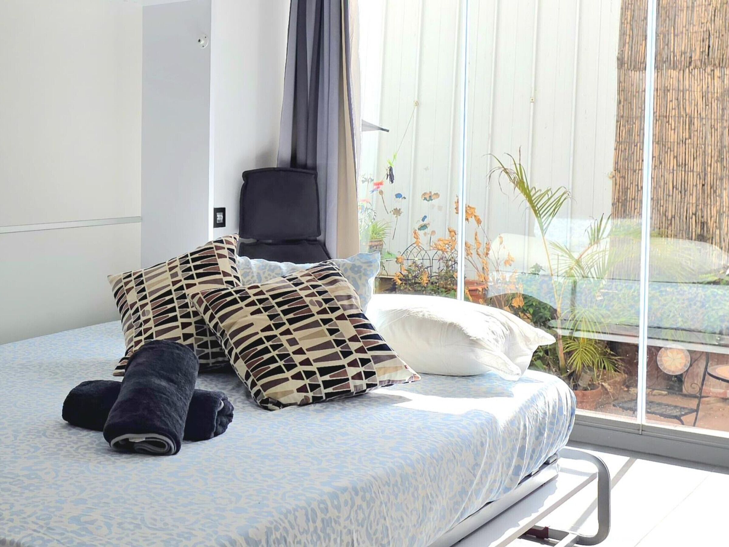A bed with patterned pillows, a rolled towel, and a bedside table with a lamp.