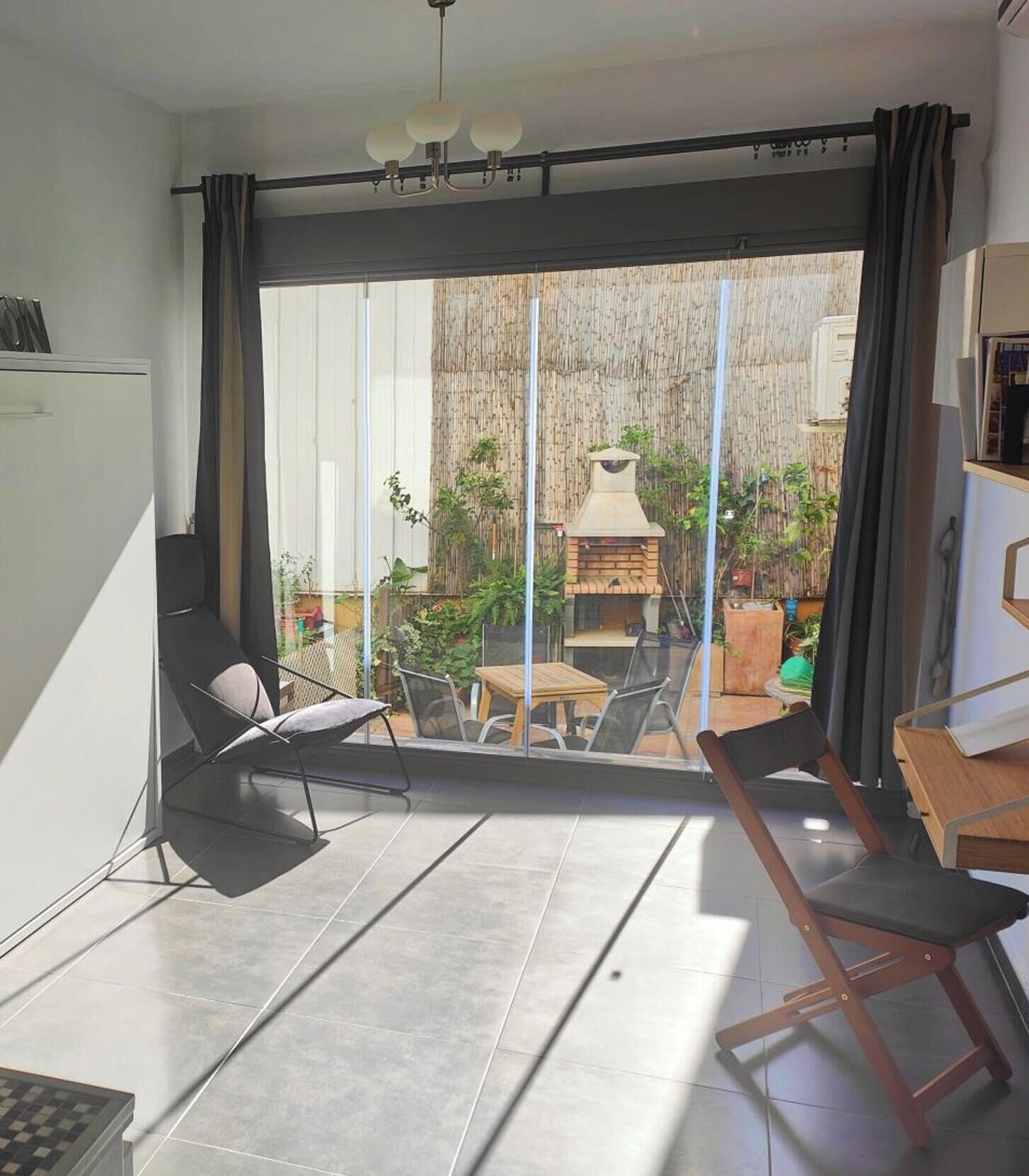 A modern living room with a large sliding glass door leading to an outdoor area with a barbecue and plants.