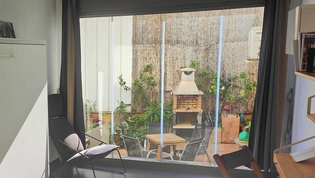 A modern living room with a large sliding glass door leading to an outdoor area with a barbecue and plants.