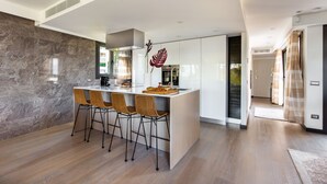 A modern kitchen with a marble backsplash, a central island with bar stools, and a large window providing natural light. - Sweet Inn - Villa Alexandra (Cannes)