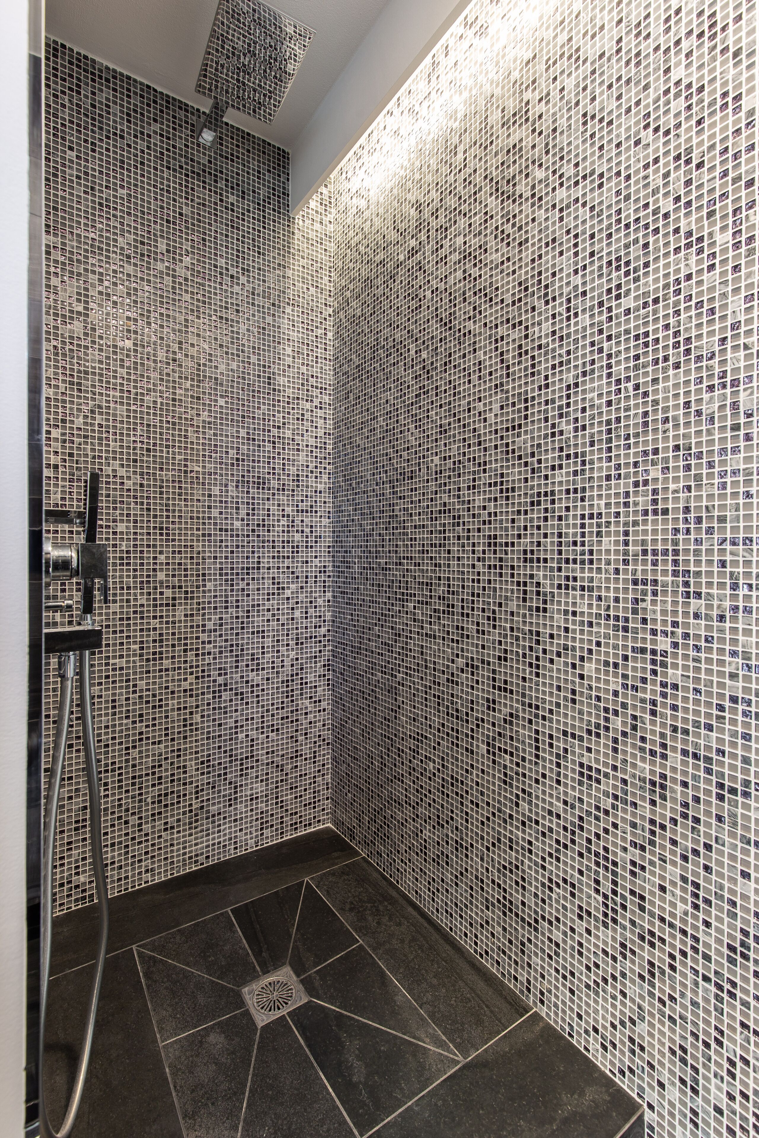 A shower area with mosaic tile walls and a drain in the center of the floor.