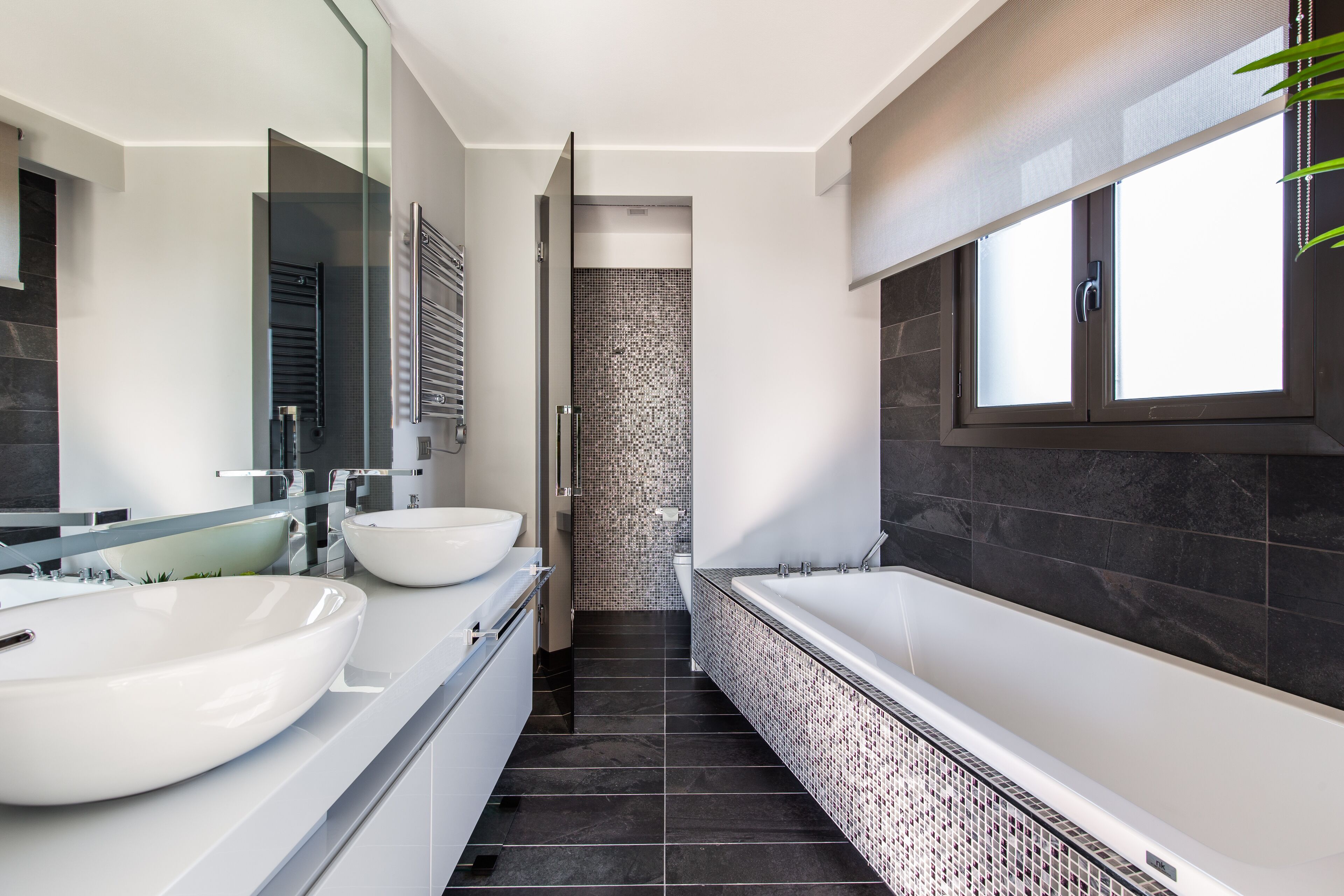 Une salle de bain moderne avec deux grands lavabos blancs, une baignoire sur pieds et une douche à l’italienne.