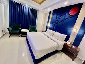 Une chambre d’hôtel avec un grand lit, deux fauteuils verts, une petite table et une table de chevet avec un téléphone.