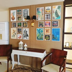 Une pièce avec une table blanche, deux chaises et un mur décoré de divers affiches et œuvres d’art encadrées.