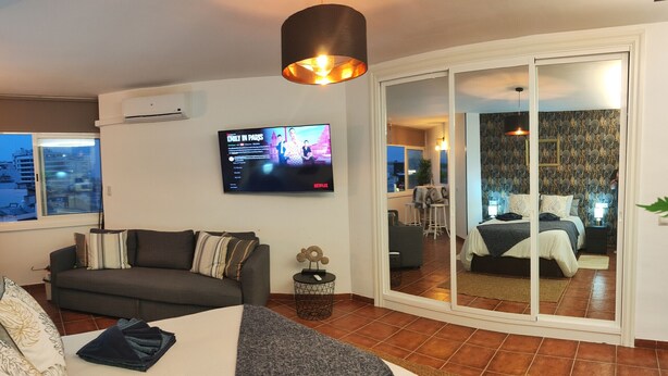 Quarto de hotel moderno com uma cama grande, um sofá, uma televisão e uma porta deslizante para uma varanda.
