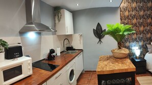 Cozinha moderna com micro-ondas, torradeira, pia e máquina de lavar. Há uma mesa de madeira com uma planta e um suporte para vinhos.