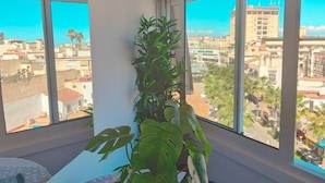 Quarto com grandes janelas, uma planta em vaso e vista para a cidade.
