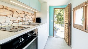 A modern kitchen with a stone backsplash, a built-in stove, and a large window. - Small rustic dream in a quiet location with a view of the mountains (Indemini)
