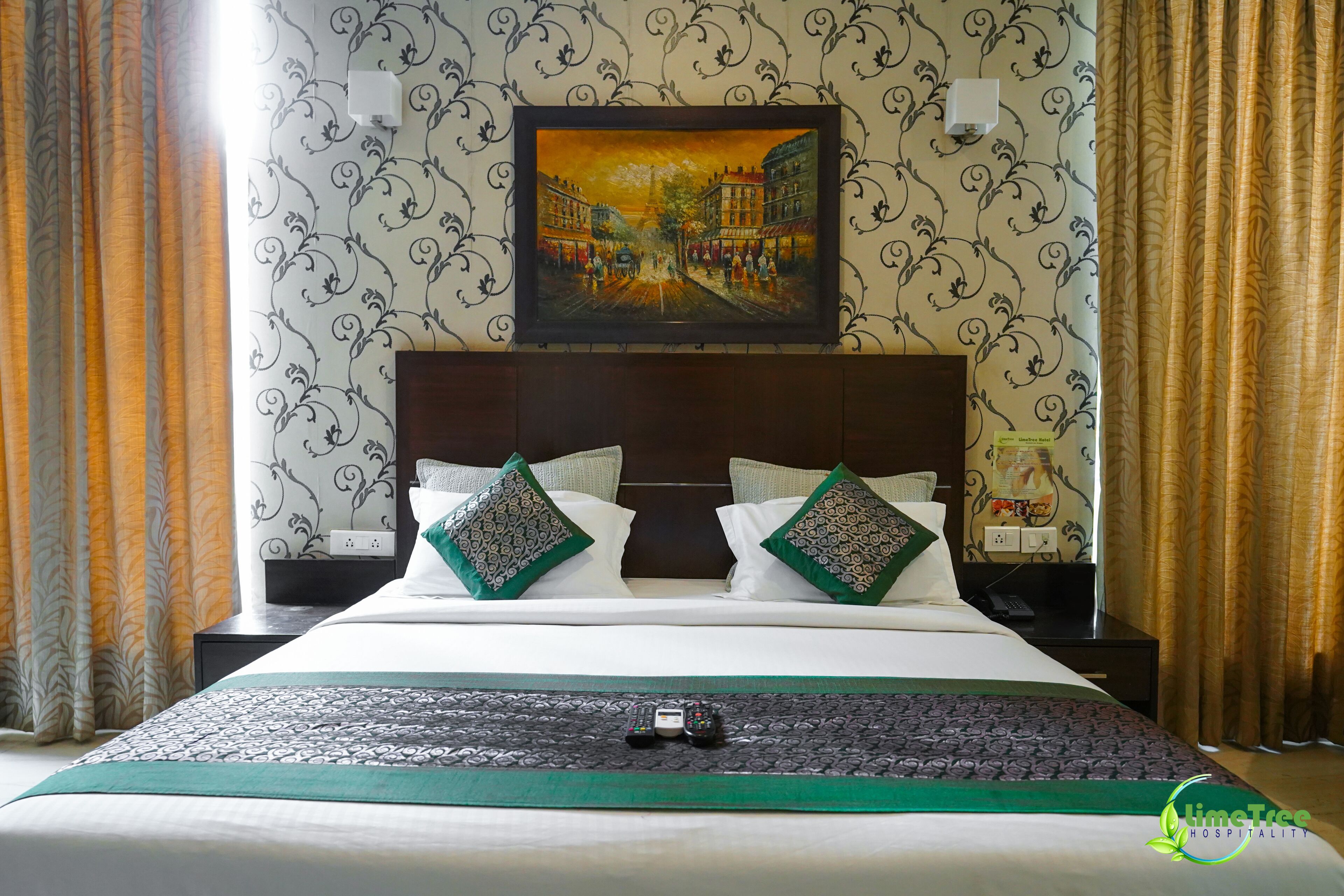 Ein Hotelzimmer mit Bett, zwei Kissen, einem Nachttisch, einem Beistelltisch, einem Bild an der Wand und Vorhängen.