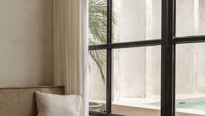 A modern interior with a beige sofa, a large window with black frames, and a view of a pool and outdoor area. - Luxe & Unique honeymoon Bocami Suites- 2 by OriVista (Kerobokan)