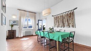 En matplats med ett grönt bordsduksklätt bord, sex stolar, en hängande lampa och utsikt över utomhusmiljön genom ett fönster.