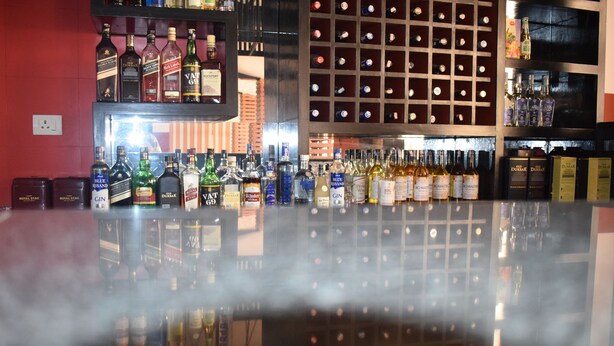 Un bar con estantes llenos de botellas de licor y un espejo que refleja la zona del bar.