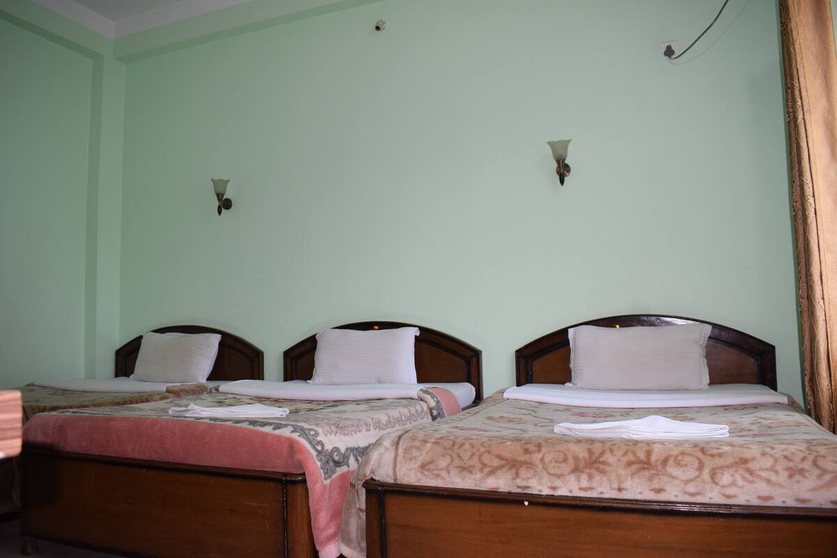 Two wooden beds with headboards, a light green wall, and a small window with curtains.