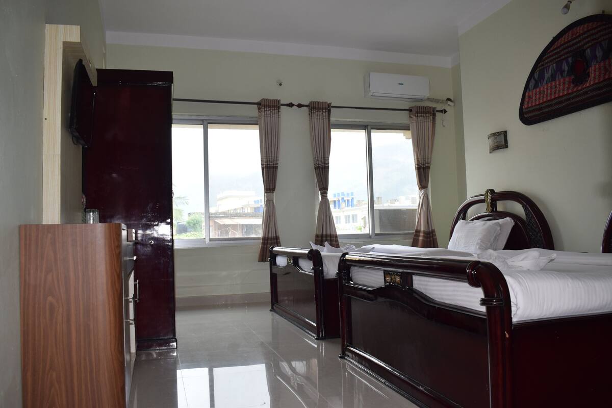 A bedroom with a bed, a wooden wardrobe, a flat-screen TV, and a window with curtains.