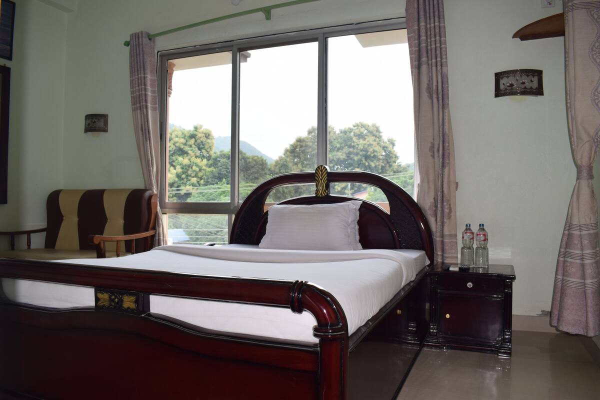 A neatly made bed with a wooden headboard, a nightstand with two bottles, and a chair.