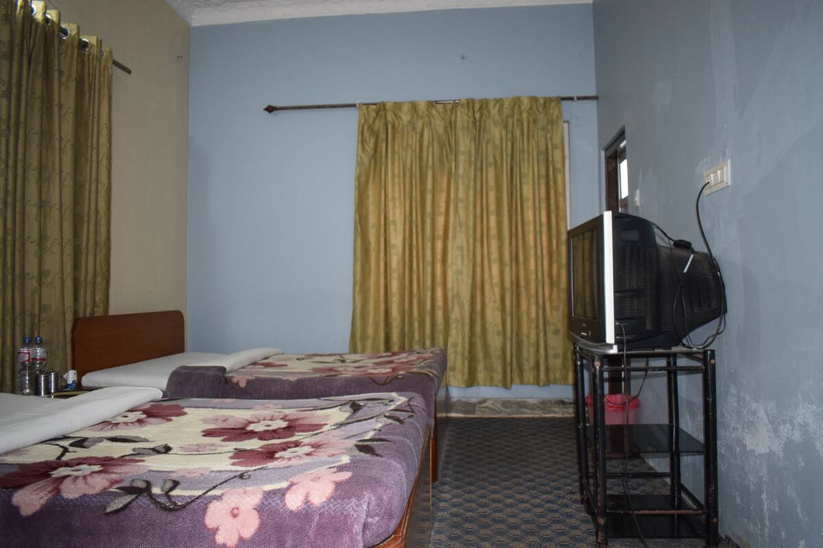 A hotel room with two beds, a television on a stand, and curtains.