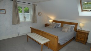Une chambre à coucher avec un lit en bois, deux tables de chevet avec des lampes, un banc, une fenêtre avec des rideaux et un radiateur.