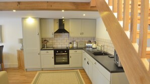 Une cuisine avec des meubles blancs, un four noir et un escalier en bois.