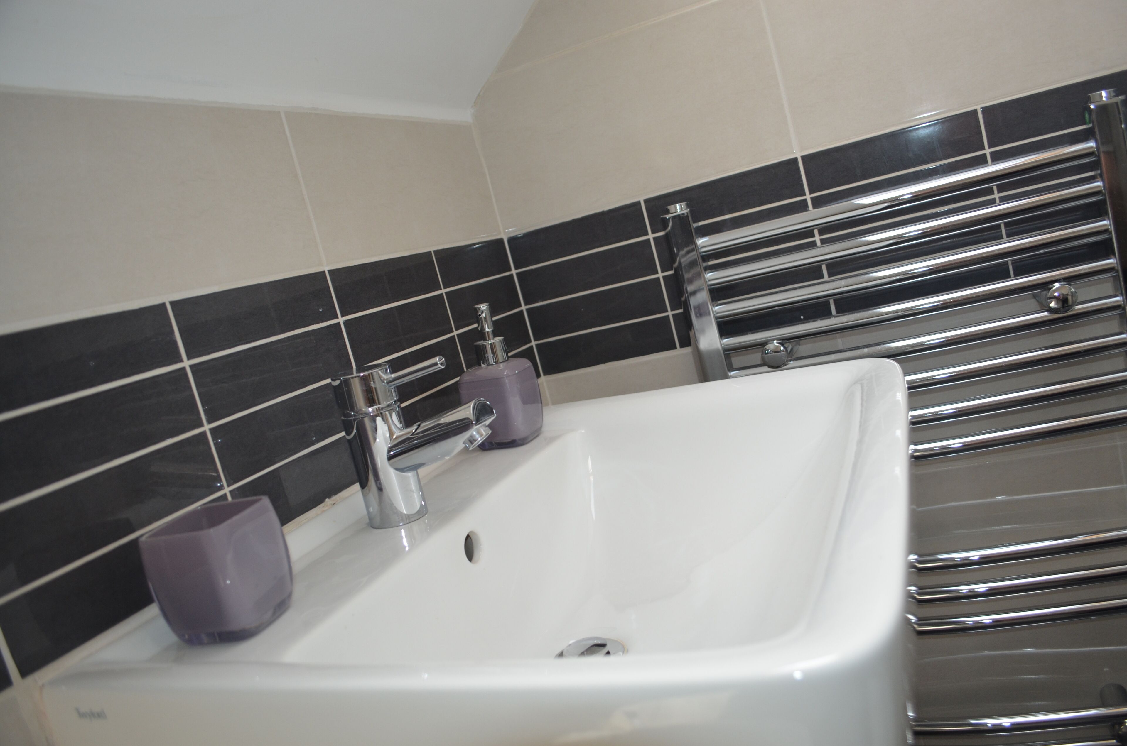 A bathroom with a white sink, chrome towel rack, and black and white tiled walls.