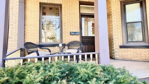 A brick building with a covered porch, two wicker chairs, and a small table. - Historic 1884 Victorian Downstairs Unit. Walk to everything! Close to elk! (Saint Marys)