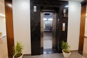 Un ascenseur situé dans un hall d’entrée aux murs de marbre et agrémenté de plantes en pot.