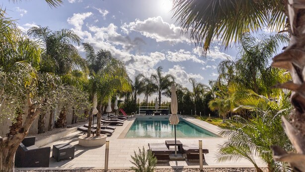 A pool area with lounge chairs and umbrellas, surrounded by palm trees and a clear sky. - VILLA SICILY SWIMMING POOL (italia,sicilia)