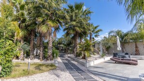 A pathway lined with palm trees leading to a seating area with a white umbrella. - VILLA SICILY SWIMMING POOL (italia,sicilia)