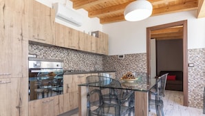 A modern kitchen with wooden cabinets, a glass dining table, and a tiled backsplash. - VILLA SICILY SWIMMING POOL (italia,sicilia)