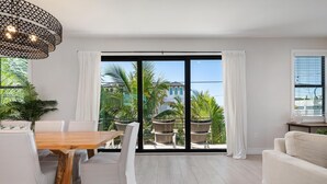 Ein modernes Wohnzimmer mit einem Holzesstisch, weißen Sofas und einer großen Schiebeglastür, die auf einen Balkon mit Gartenmöbeln führt.
