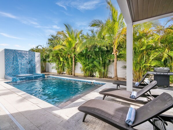 A swimming pool with a blue mosaic wall, surrounded by palm trees and lounge chairs.