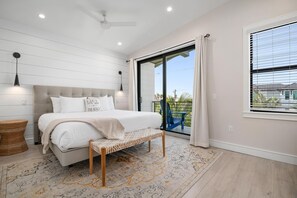 A bedroom with a bed, bench, ceiling fan, and a view of the outdoors.