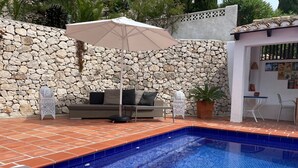 A swimming pool with a stone wall and a seating area with a table and chairs.
