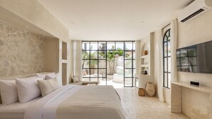Ein modernes Schlafzimmer mit einem großen Bett, einem Fernseher und Blick auf einen Garten durch eine Glastür.