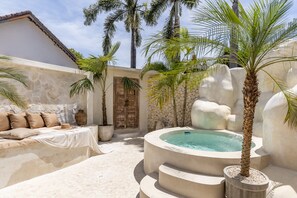 Un espace spa comprenant un jacuzzi, un mur en pierre et un lit agrémenté d’oreillers de couleur beige.