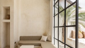 Eine Sitzecke mit gepolstertem Sitz und kleinem Tisch, ein Fenster mit Blick auf Palmen und ein Steingartenbehälter.