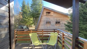 Une terrasse en bois avec deux fauteuils de jardin verts, une cabane en bois en arrière-plan et un ciel dégagé.