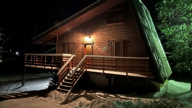 Une cabane en bois avec un escalier menant à l’entrée, entourée de neige.
