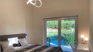 Un dormitorio con cama, mesita de noche y vista a un jardín a través de una puerta corrediza de vidrio.