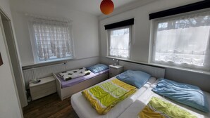 A bedroom with a bed, bedside tables, a window with curtains, a radiator, and a hanging lamp. - Old kindergarten - now home to Baltic Sea vacationers (Fuhlendorf)