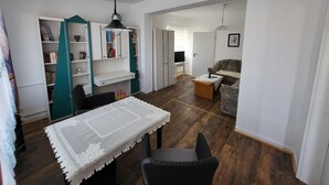 A dining area with a table and chairs, a bookshelf, a sofa, and a television in the background. - Old kindergarten - now home to Baltic Sea vacationers (Fuhlendorf)