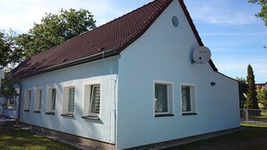 A white building with a red roof, multiple windows, and a satellite dish. - Old kindergarten - now home to Baltic Sea vacationers (Fuhlendorf)