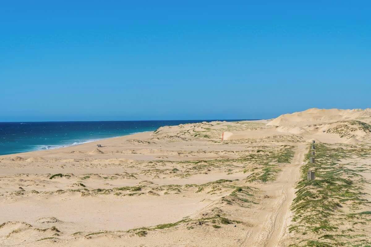 A sandy beach with a clear blue sky and a distant view of the ocean.