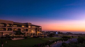 A large, multi-story hotel with a well-maintained lawn and a view of the ocean at sunset.