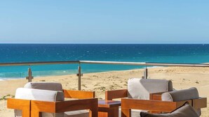 Un espace aménagé avec des chaises en bois et une table, situé au bord de la plage et offrant une vue sur l’océan bleu et la plage de sable fin.